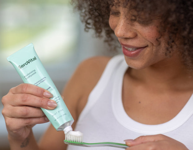 Woman applying toothpaste to a toothbrush with a SeroVital toothpaste tube.