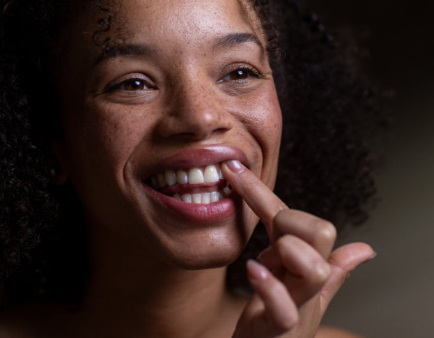 Woman smiling with one hand on her gums against a dark background