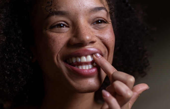 Close-up of a woman smiling with her hand near her mouth against a dark background