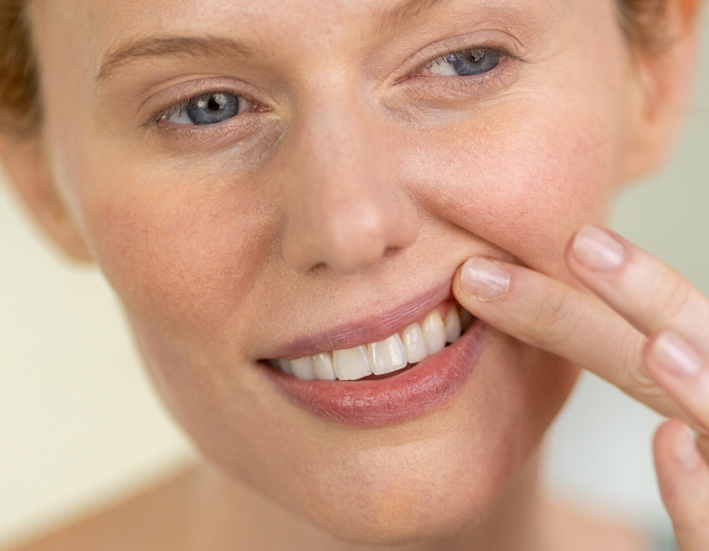 Woman with a finger on her cheek, possibly indicating skin texture or concern.