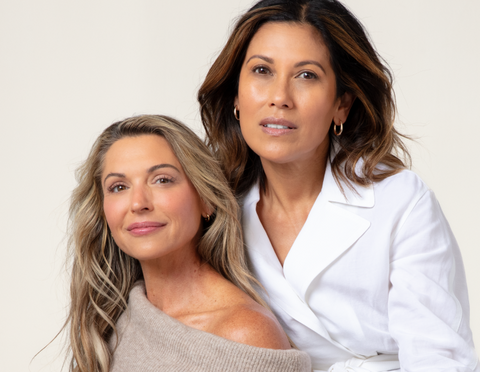 This is a portrait of two women standing close together against a plain, light background.