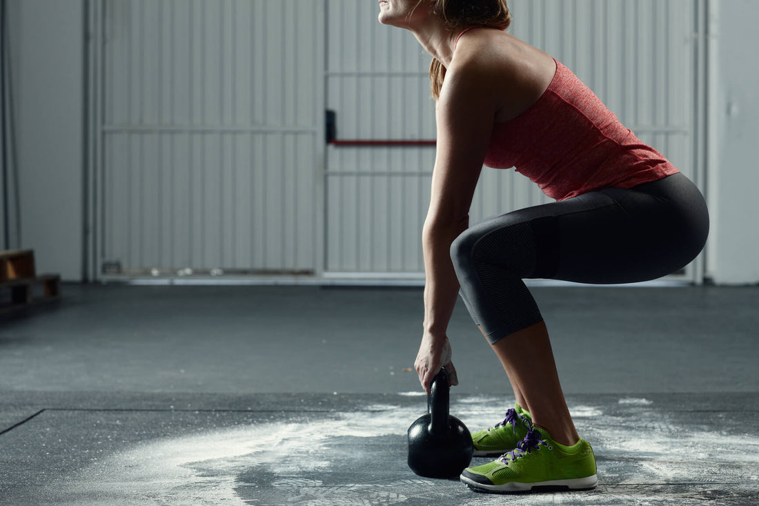 Athletic white woman in workout clothes  doing squats with a kettle bellAthletic white woman in workout clothes  doing squats with a kettle bell