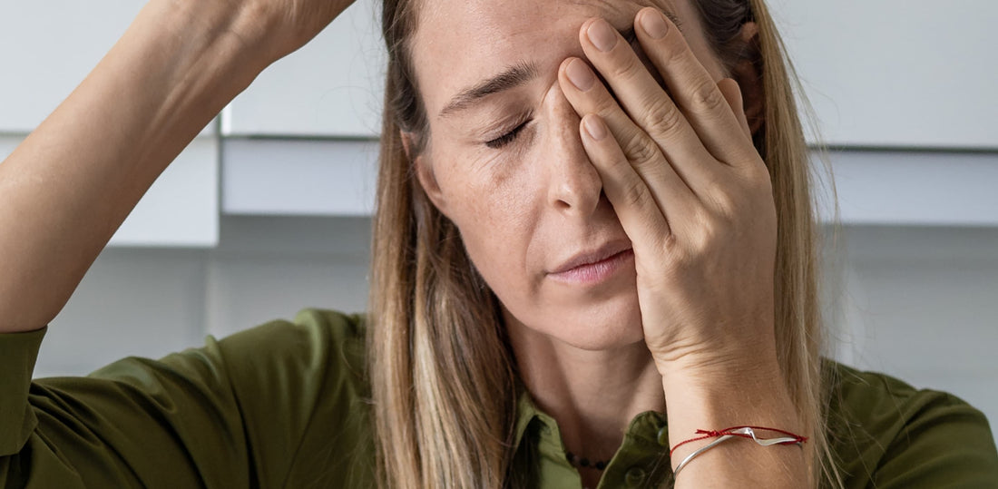 Woman with her eyes closed, one hand covering her eye and the other resting on her head. 