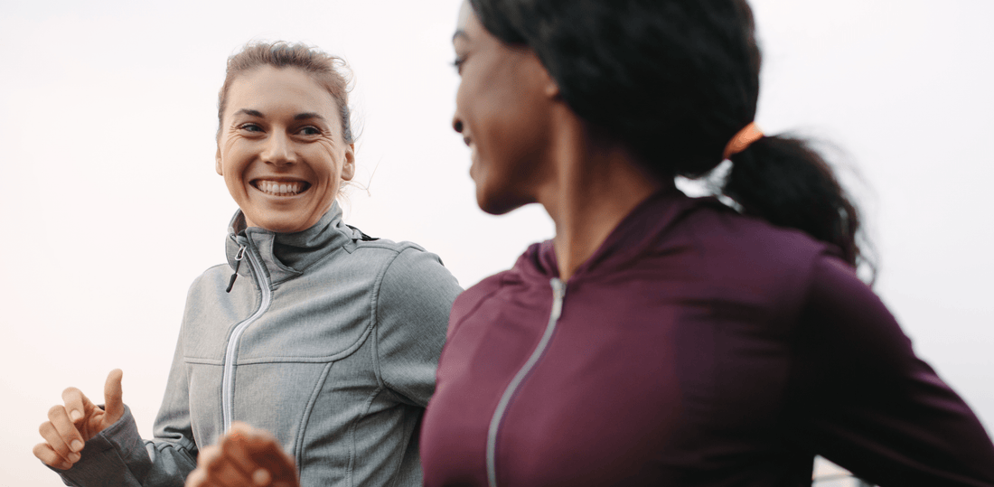 Two women in athletic wear smiling and running outdoors.