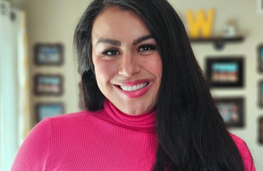 A woman with long, straight black hair, wearing a bright pink turtleneck sweater, smiles at the camera.
