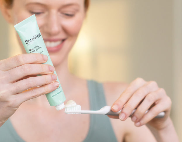 Person holding a tube of Serovital toothpaste and a toothbrush with toothpaste on it.