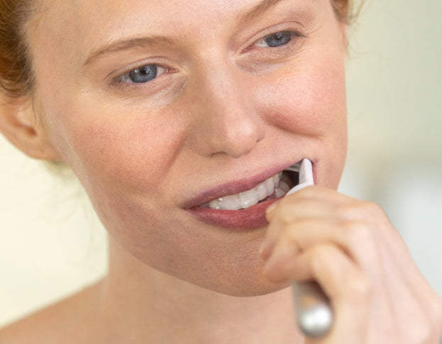 Woman brushing her teeth with a toothbrush against a plain background