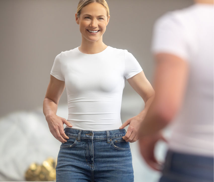 Woman wearing a white t-shirt and blue jeans standing in a neutral setting.