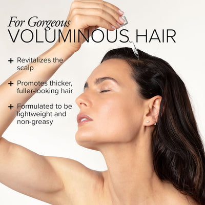 A white woman with long, thick brown hair applying a dropper of hair serum