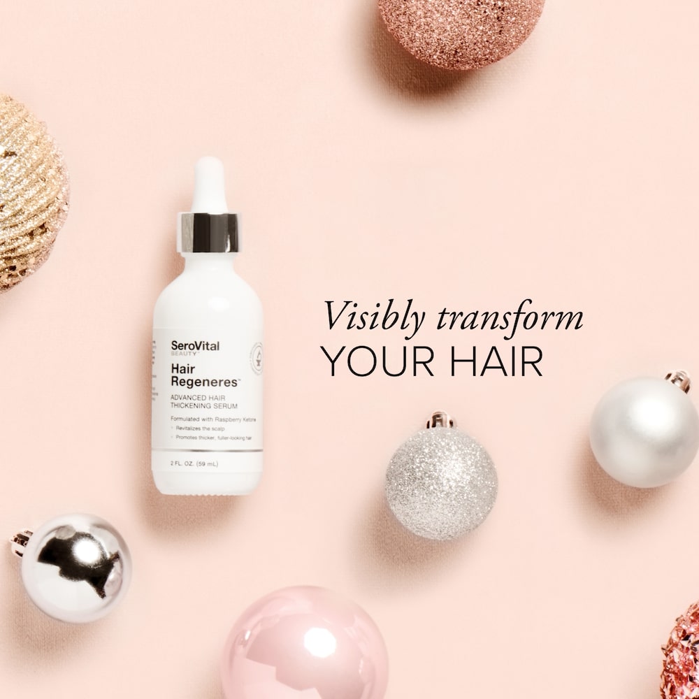 A bottle of hair serum Hair Regeneres on a pink background with holiday ornaments and text that says Visibly transform your hair