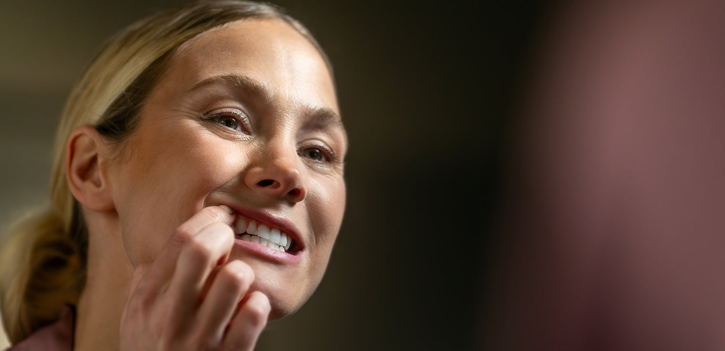 Woman with a ponytail showing her strong gums against a dark background