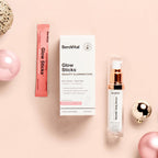 A box of anti-aging powder Glow Sticks with a pink Glow Sticks packet next to a tube of retinoid serum RetinAll Daily Serum on a pink background with holiday ornaments