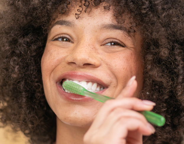 Person brushing teeth with a green toothbrush against a neutral background