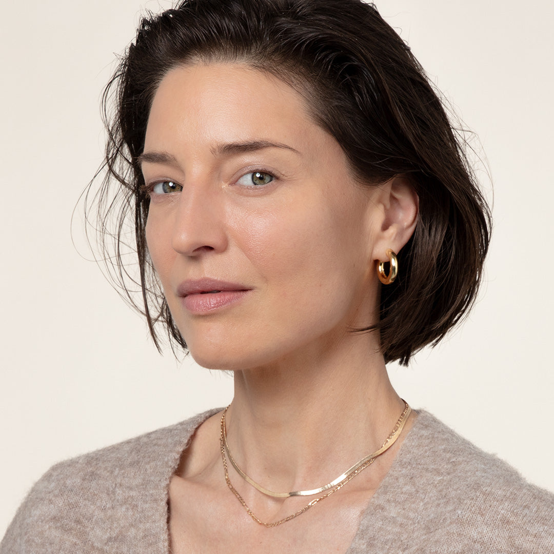 A middle-aged white woman with brown hair and gold hoop earrings looking at the camera
