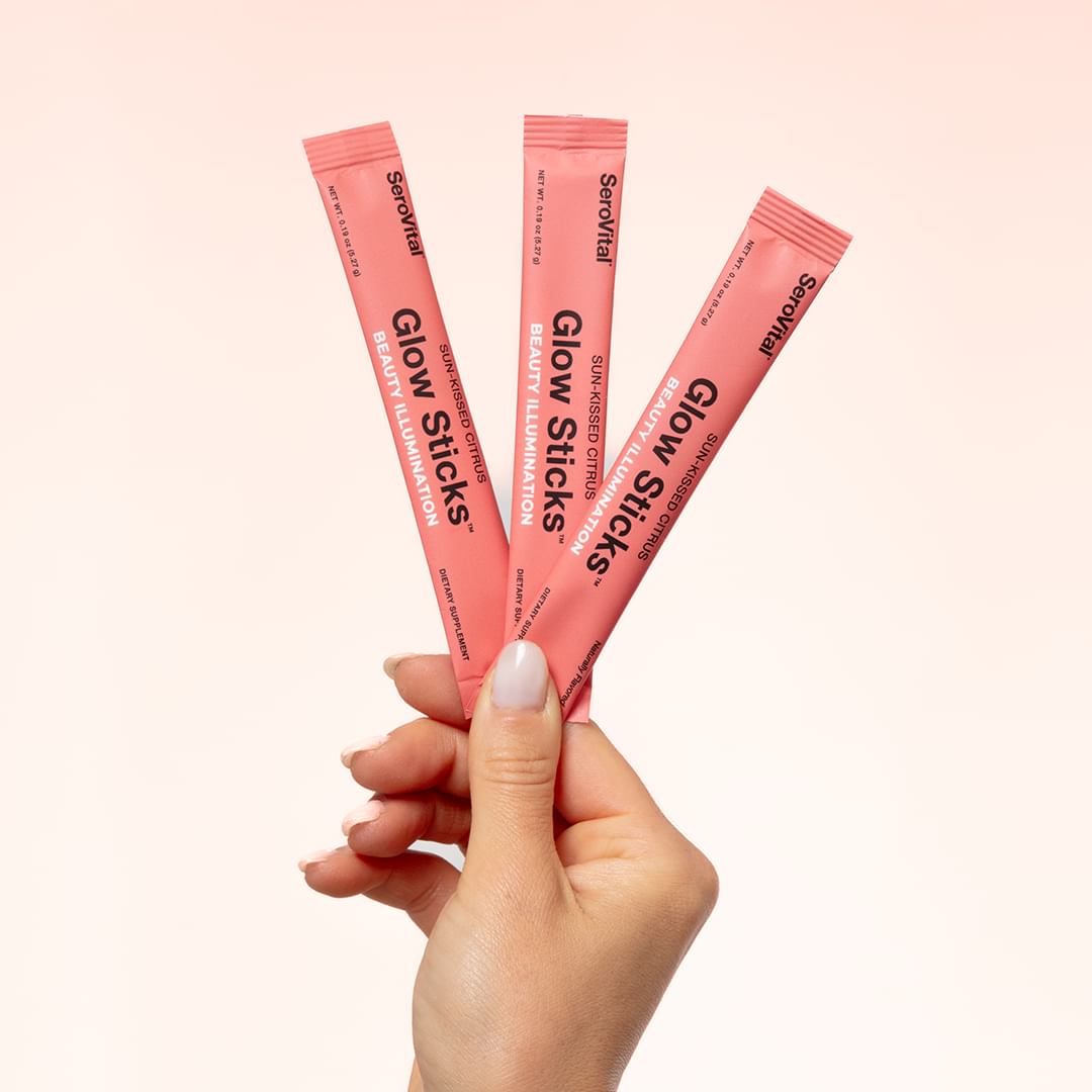 A hand with manicured fingernails holding up three packets of Glow Sticks. 