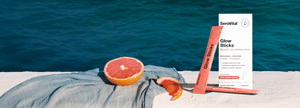 Grapefruit and SeroVital Glow Sticks on a gray towel, with a bright blue ocean in the background.