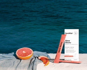 Grapefruit and SeroVital Glow Sticks on a gray towel, with a bright blue ocean in the background.