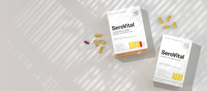 Two white boxes of SeroVital Advanced supplements and scattered capsules (yellow, white, pink) are shown on a light gray surface with window shadow patterns.