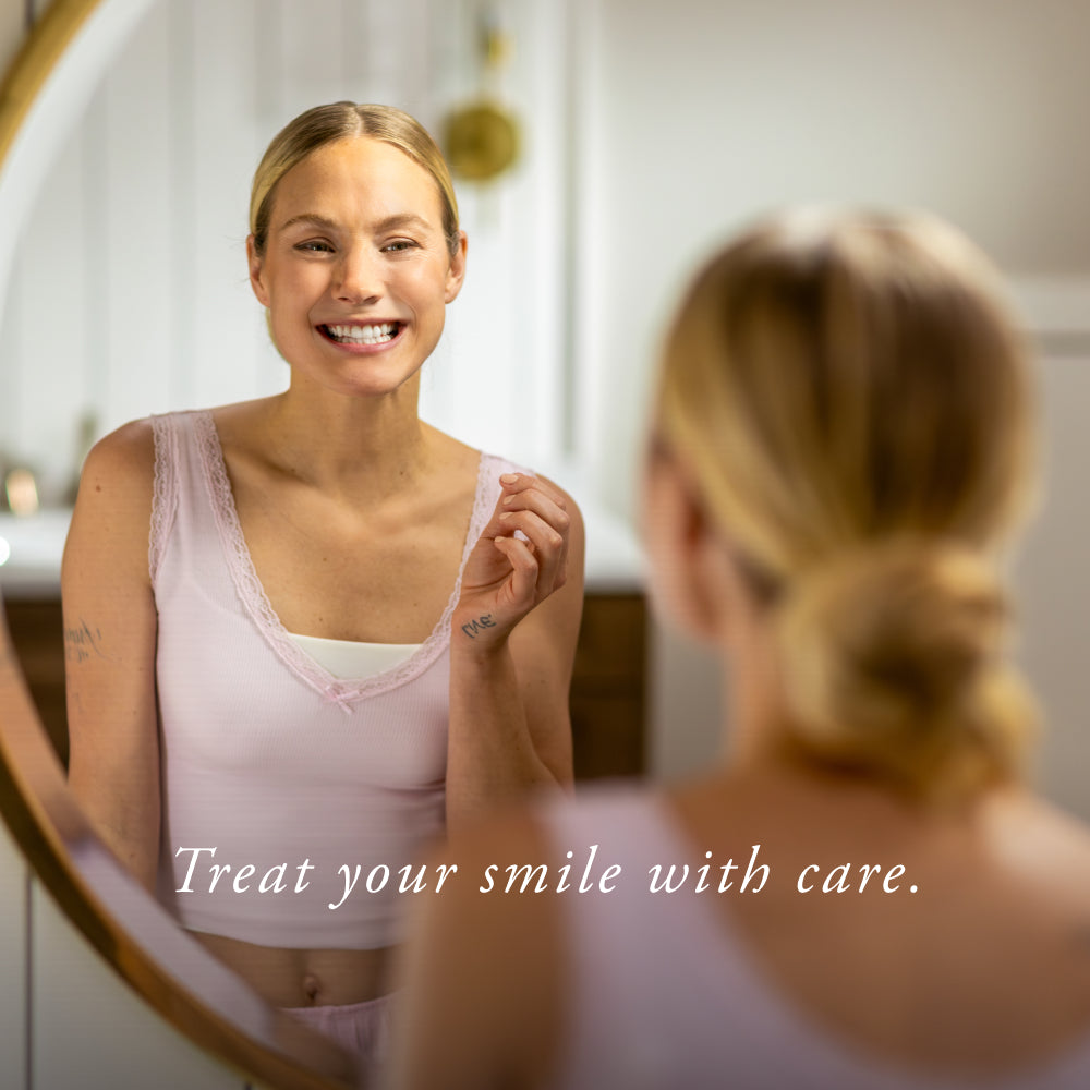 Woman looking at herself in the mirror with a smile, wearing a pink tank top.