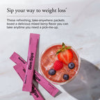 Pink Slim Sips weight loss packets arranged on a light marble surface next to a glass of pink iced drink with strawberries and blueberries. Text at the top reads 'Sip your way to weight loss'.