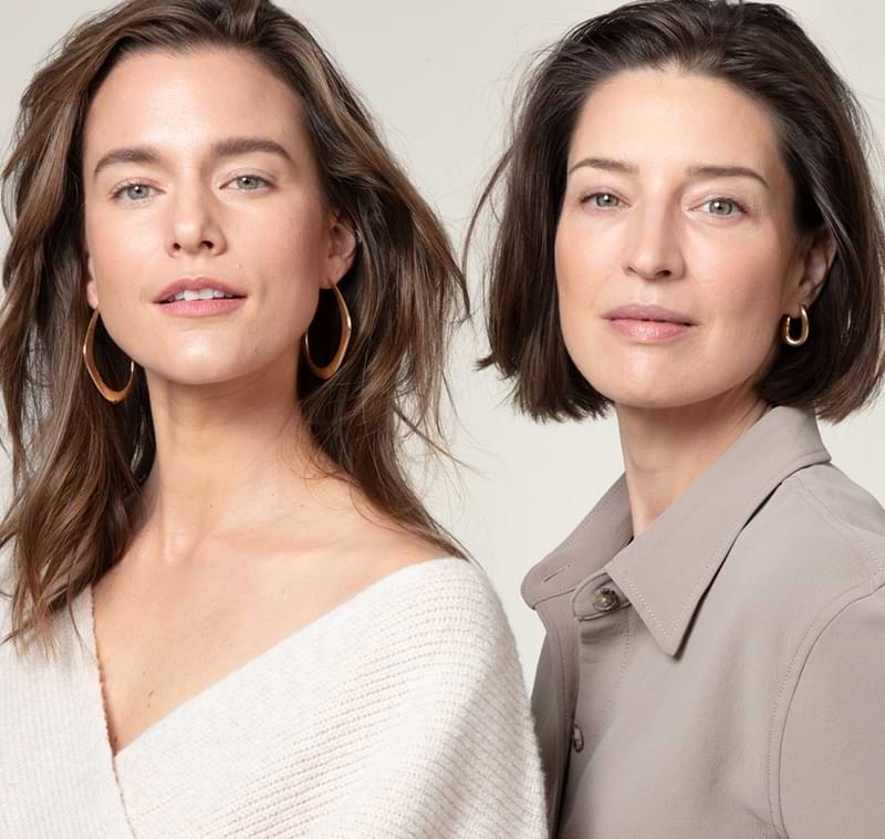 Two white women with brown hair and radiant skin sitting next to each other