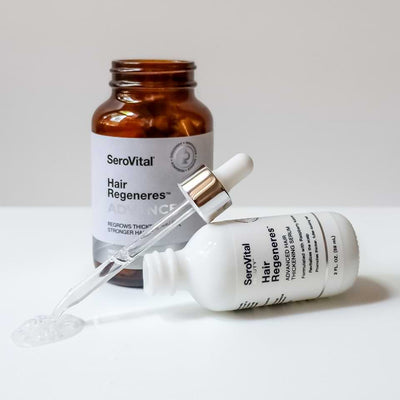 A bottle of Hair Regeneres ADVANCED with the lid off, next to a bottle of Advanced Hair Thickening Serum tipped on its side and showing the serum texture