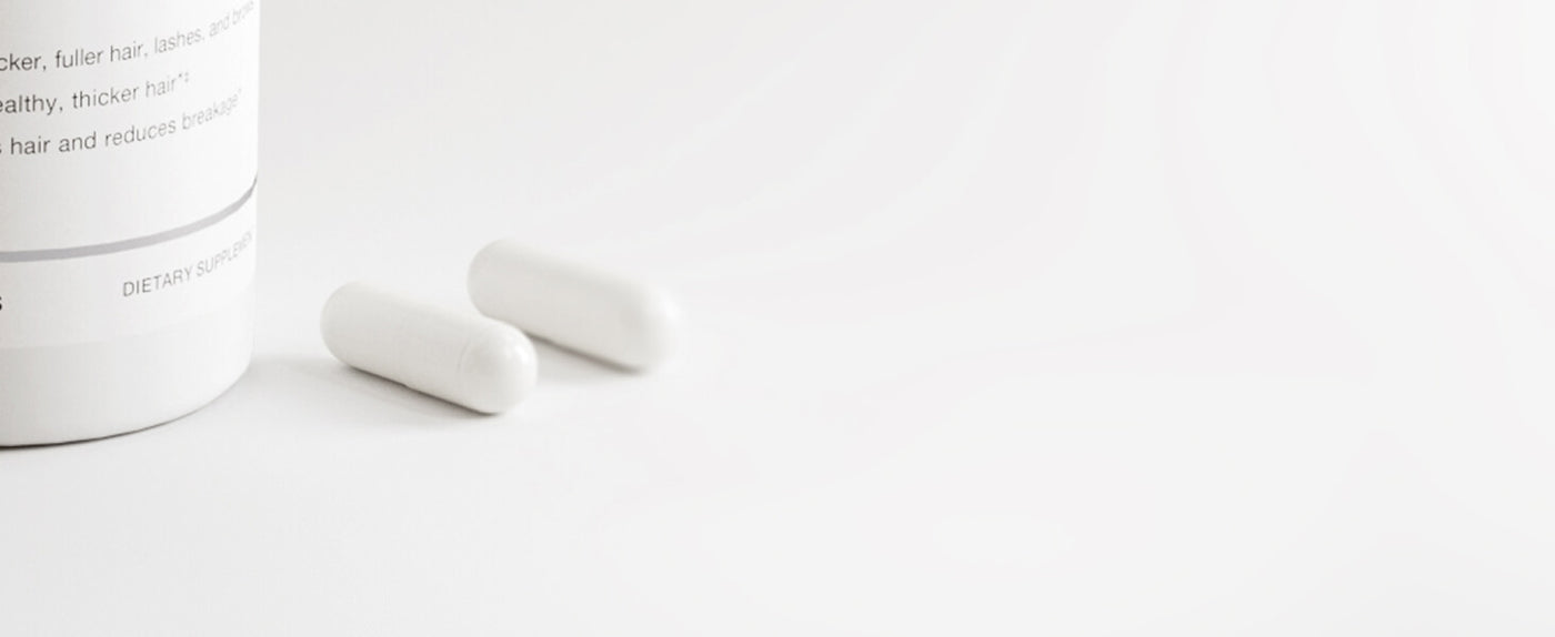 Two white pills on a light gray background with a container partially visible.