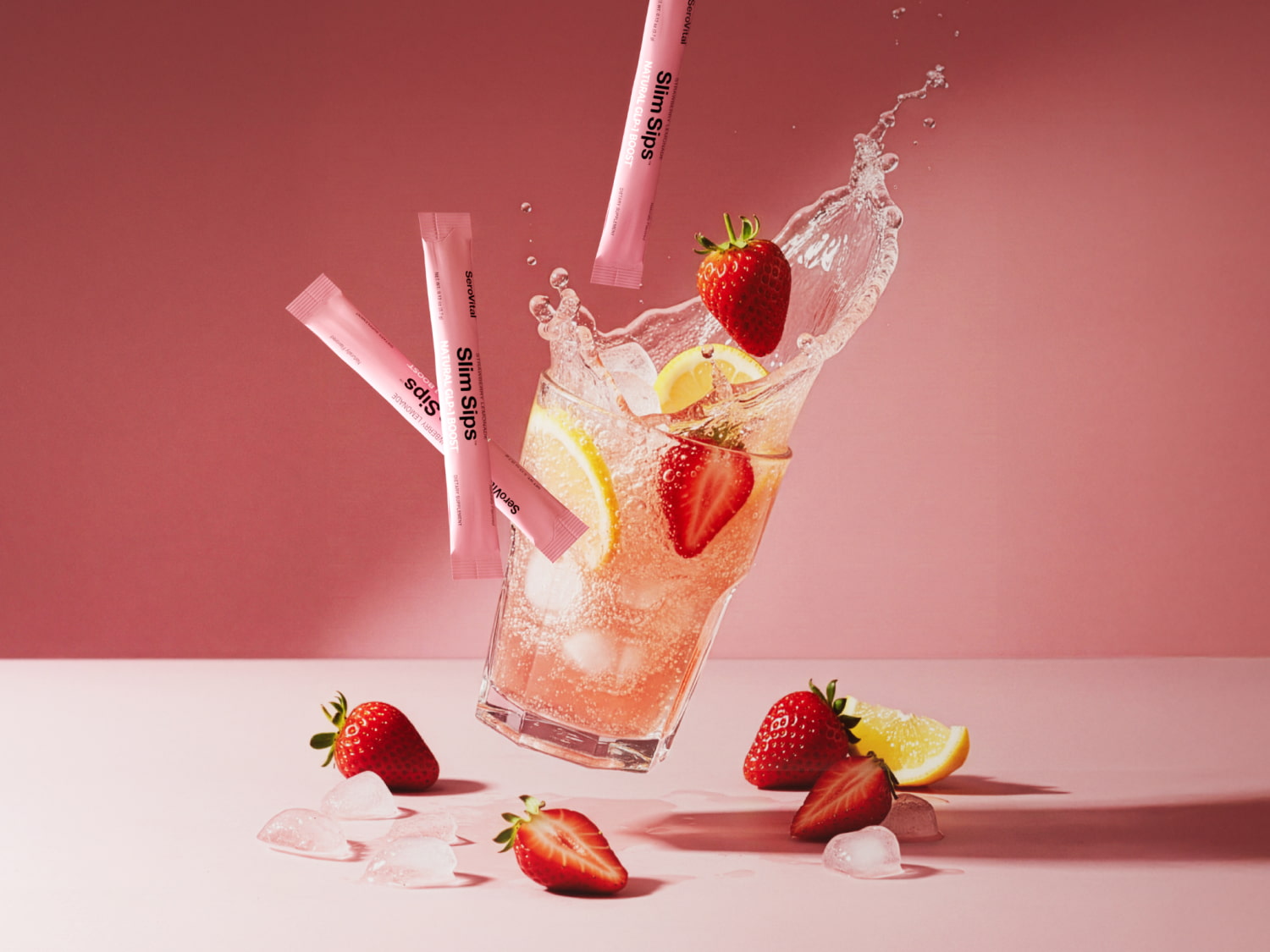 Glass of strawberry lemonade with ice, strawberries, and lemon slices on a pink background.