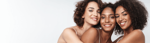 Three smiling women of diverse ethnicities embracing, showcasing healthy, glowing skin.