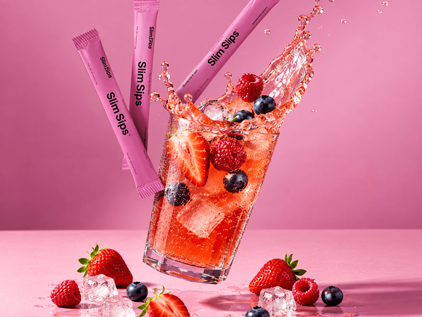 Three pink Slim Sips sachets are shown with a clear glass of pink iced beverage splashing out, decorated with strawberries, blueberries, and ice, on a pink background.