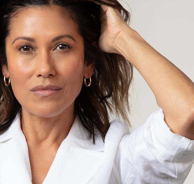 A beautiful Latina woman with gold earrings staring into the camera with her hands in her hair