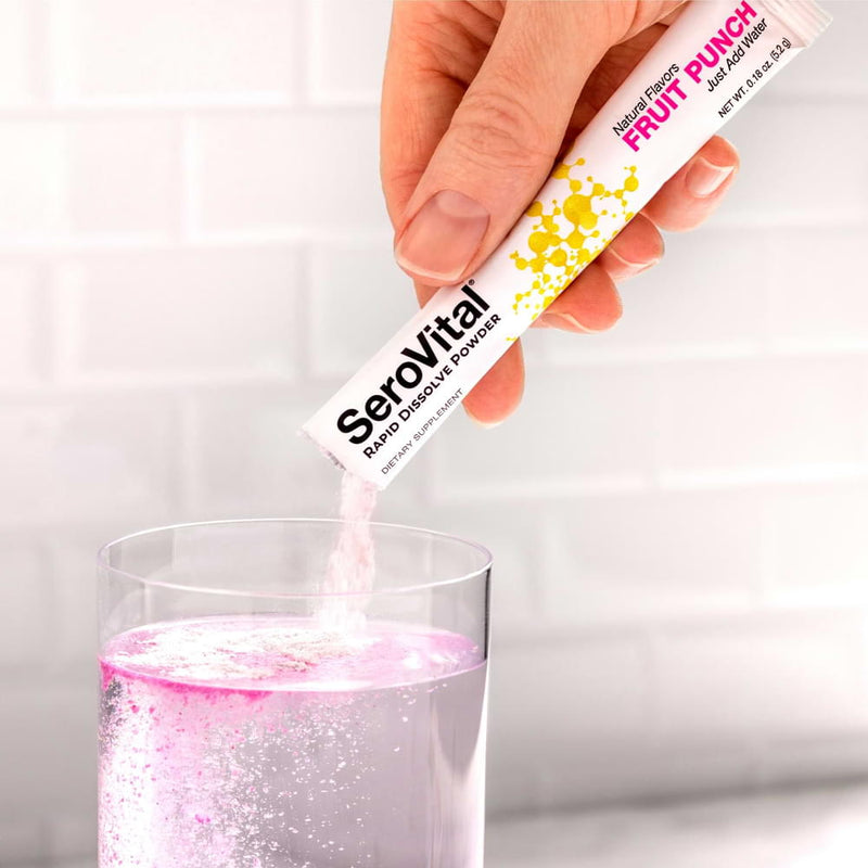 A hand pouring a packet of pink SeroVital Rapid Dissolve Powder into a glass of water