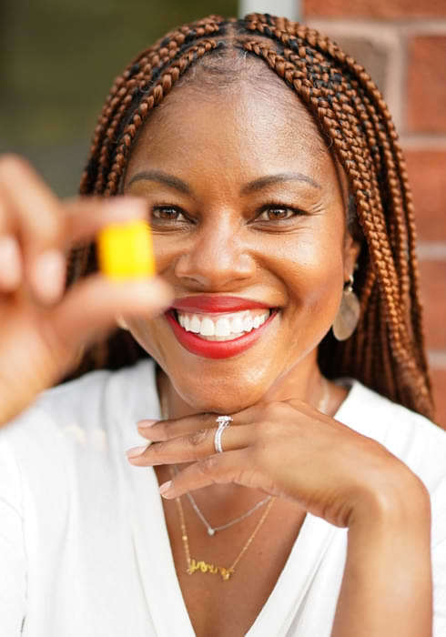 A gorgeous black woman with braided hair smiling for the camera and showcasing HGH-booster Serovital pills in her hand