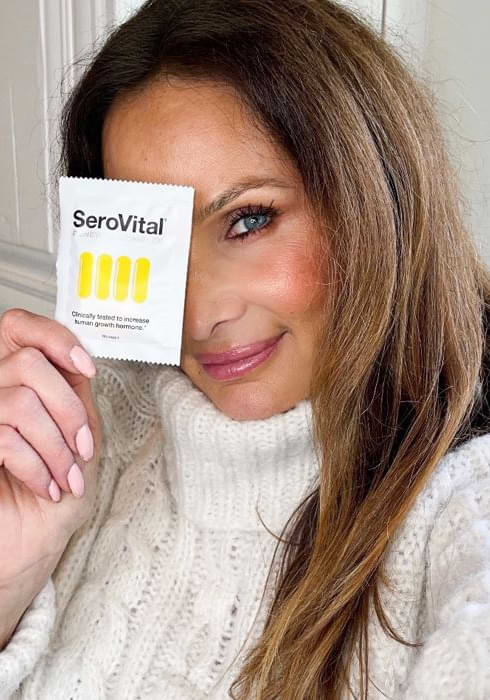 A middle-aged white woman with long brown hair holding a SeroVital sachet in front of her face