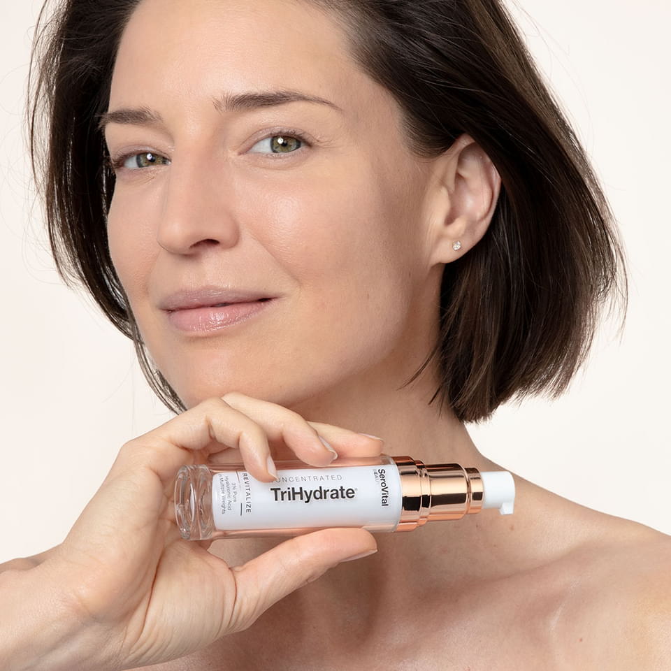 A white woman with short brown hair holding up a bottle of Trihydrate