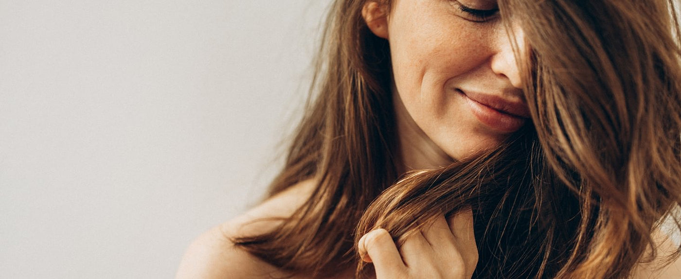 Woman with long brown hair touching her hair against a neutral background