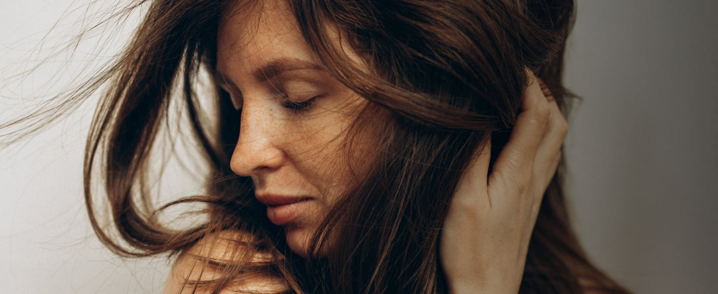 Woman with long brown hair touching her face against a neutral background